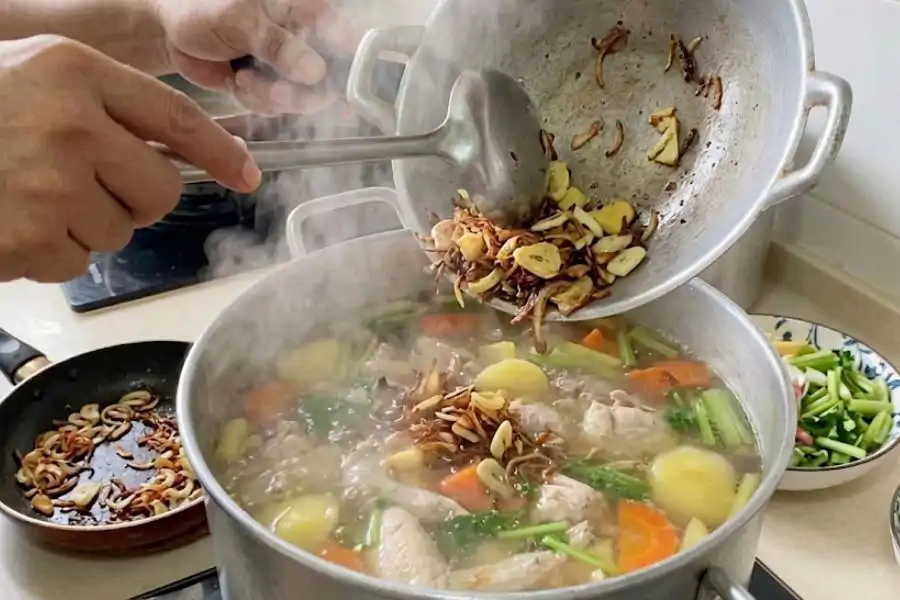 Ayam direbus sehingga empuk sebelum bahan tumis dan daun sup dimasukkan pada akhir proses memasak. Gambar AI